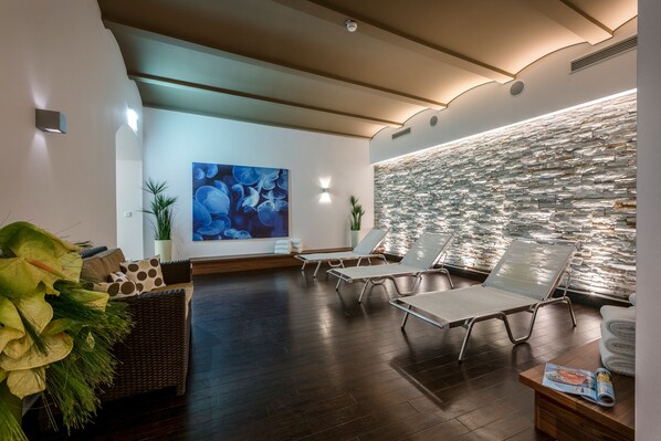 Un moderno cuarto de spa con pared de piedra, sillones de descanso, un amplio cuadro abstracto y un sofá de mimbre.
