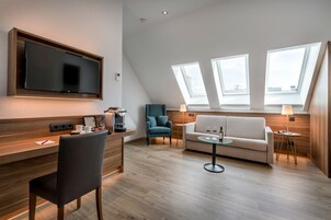 A modern living room with a flat-screen TV, a sofa, a coffee table, and a dining area with a chair and a small table.