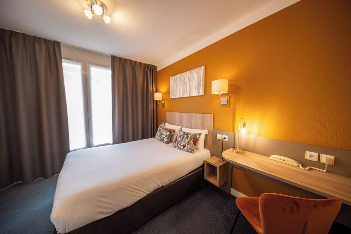 Une chambre d’hôtel avec un grand lit, une table de chevet avec une lampe, un téléphone et une chaise.