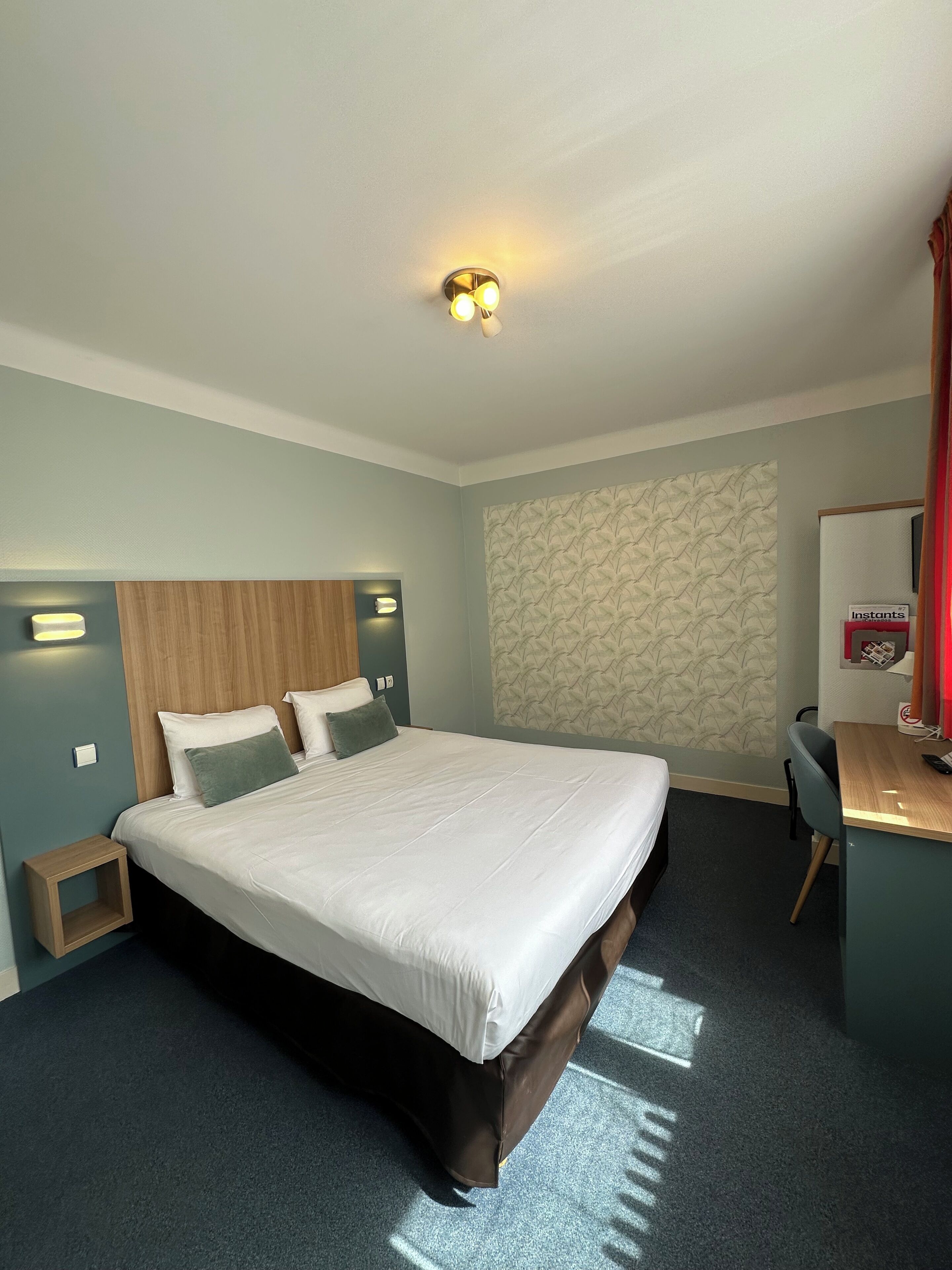 Habitación de hotel con una cama grande, cabecera de madera, escritorio con una silla y pared con papel tapiz estampado.