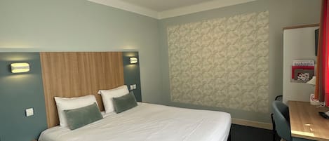 Habitación de hotel con una cama grande, cabecera de madera, escritorio con una silla y pared con papel tapiz estampado.