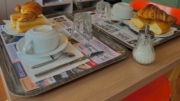 A breakfast tray with croissants, a cup of coffee, and a glass of milk on a table with a newspaper. - Hôtel de Caen (Caen)