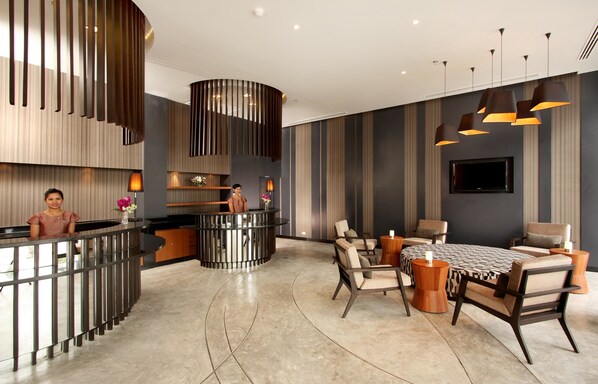 A modern hotel lobby with a reception desk, seating area, and a large flat-screen TV.