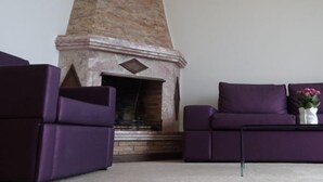 A living room with a stone fireplace, two purple sofas, and a small table with a vase of flowers. - Beach Hotel Split (Podstrana)