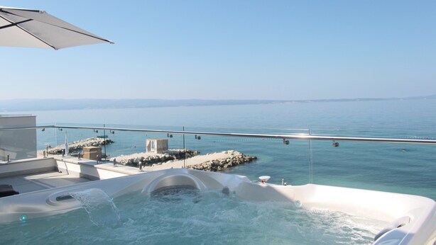 A hot tub on a balcony with a clear view of the sea and rocky shoreline. - Beach Hotel Split (Podstrana)