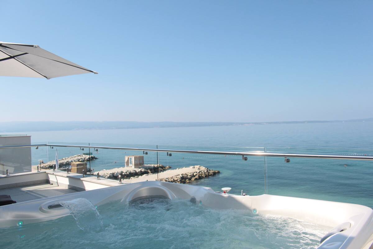 Un bain à remous sur un balcon offrant une vue dégagée sur la mer et le littoral rocheux.