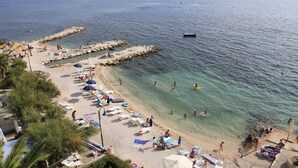 A beach with clear waters, sun loungers, umbrellas, and a rocky breakwater. - Beach Hotel Split (Podstrana)