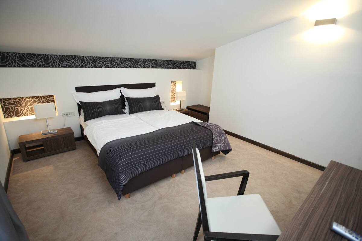 Une chambre d’hôtel moderne avec un grand lit, deux tables de chevet, une chaise et un bureau.