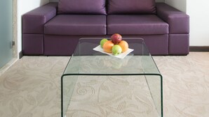 A modern living room with a purple sofa, a glass coffee table with fruit, and a potted orchid on a white shelf. - Beach Hotel Split (Podstrana)