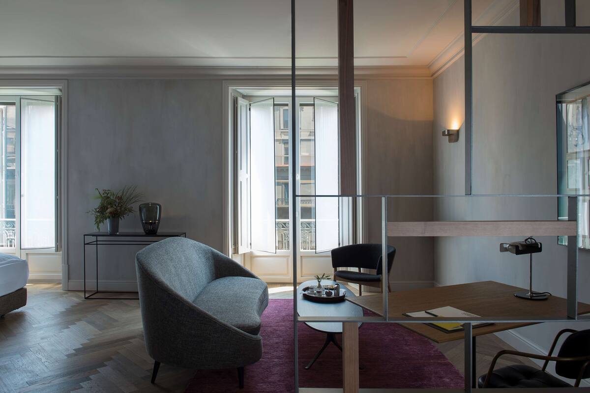 Una habitación de hotel moderna con una cama, un escritorio, una silla, una mesita con una bandeja y una planta en maceta.
