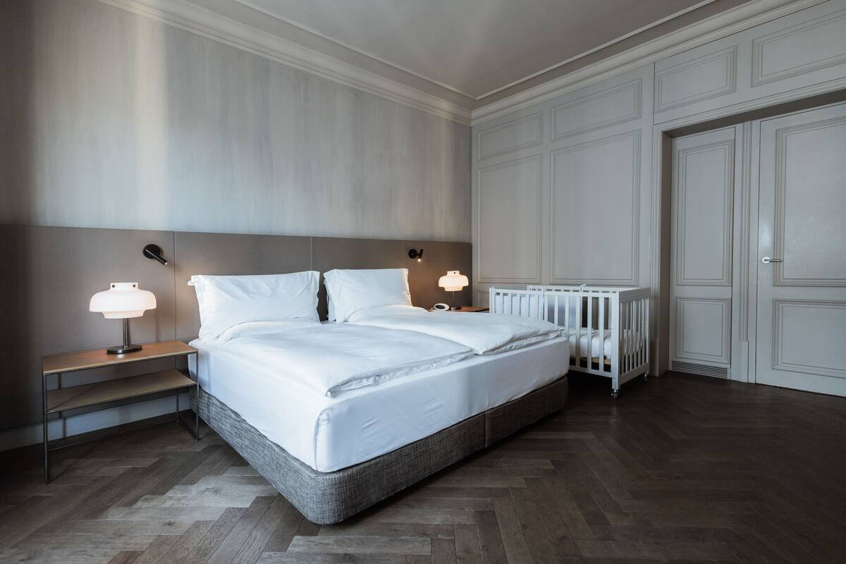 Un dormitorio con una cama grande, dos mesitas de noche con lámparas, un radiador blanco y un armario blanco.