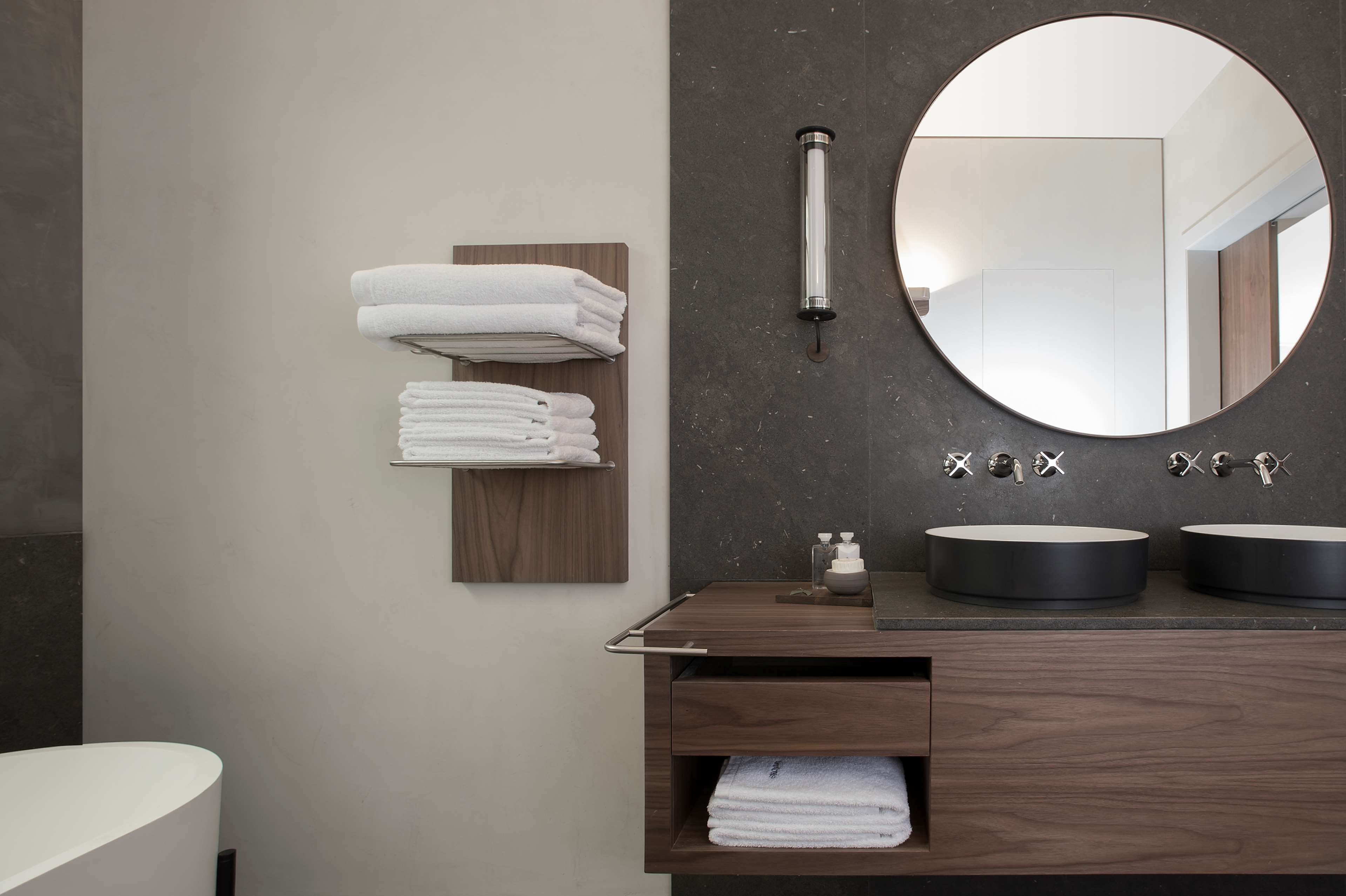 A modern bathroom with a wooden vanity, two round black sinks, a large mirror, and neatly stacked white towels.