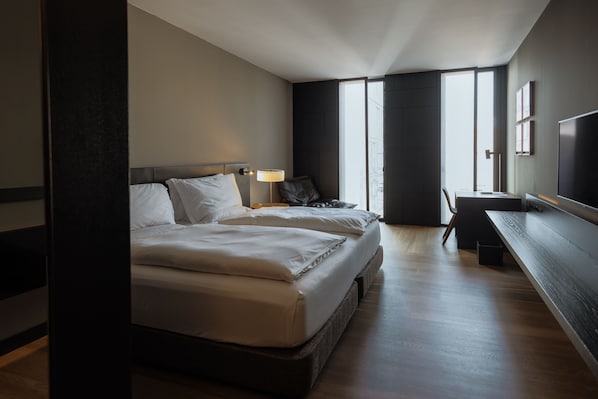 A modern hotel room with a large bed, bedside tables, a desk, and a TV.