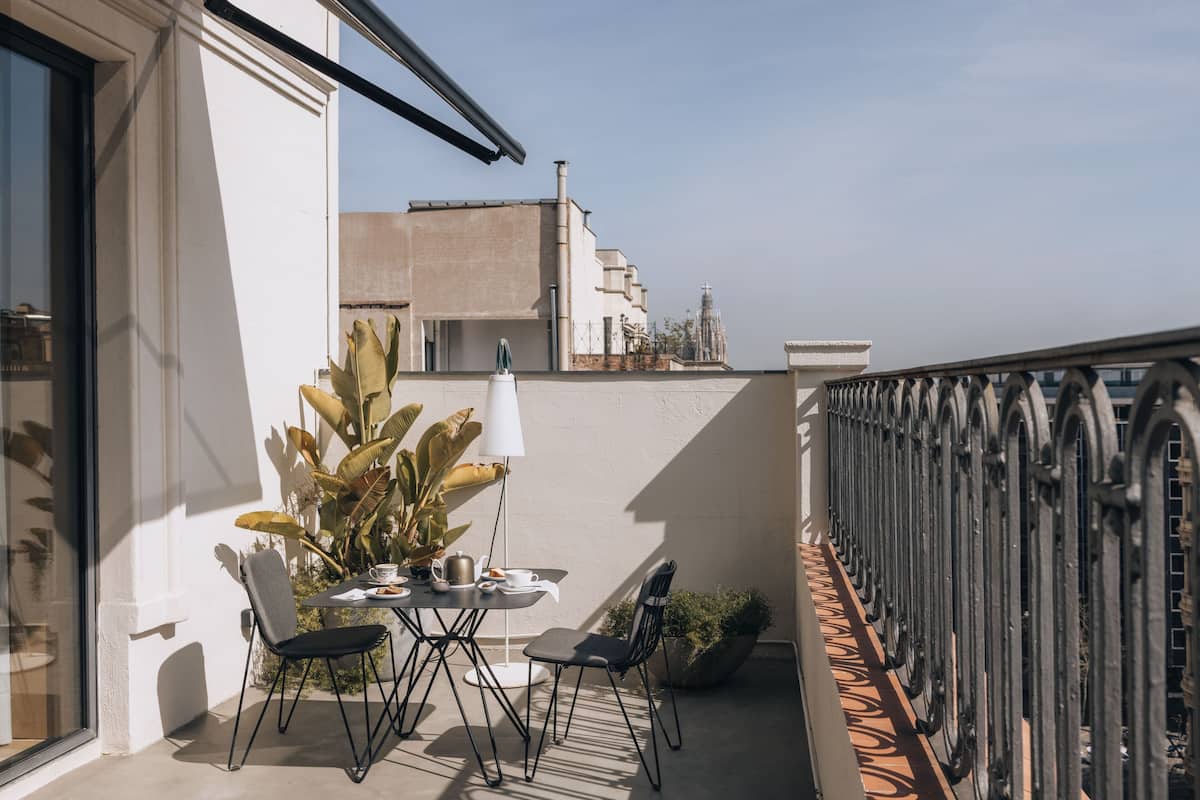 Un balcón con una mesa y sillas, una planta en maceta y vistas de edificios al fondo.
