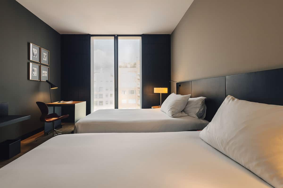 Habitación de hotel con dos camas, un escritorio, una silla y un ventanal grande.