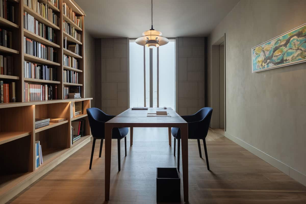Una biblioteca moderna con una mesa de madera, sillas negras y una amplia estantería.