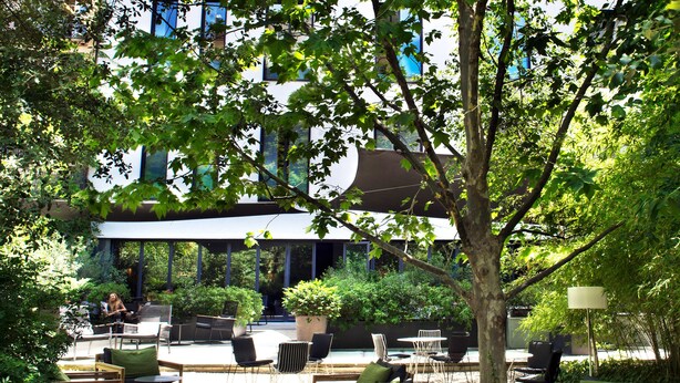 An outdoor seating area with wooden furniture and a large tree. - Alma Barcelona GL (Barcelona)