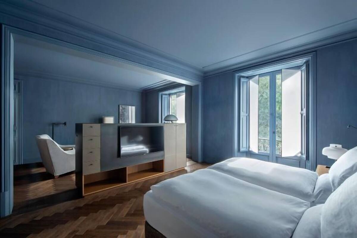 Un dormitorio con cama, escritorio, silla y ventanas amplias.