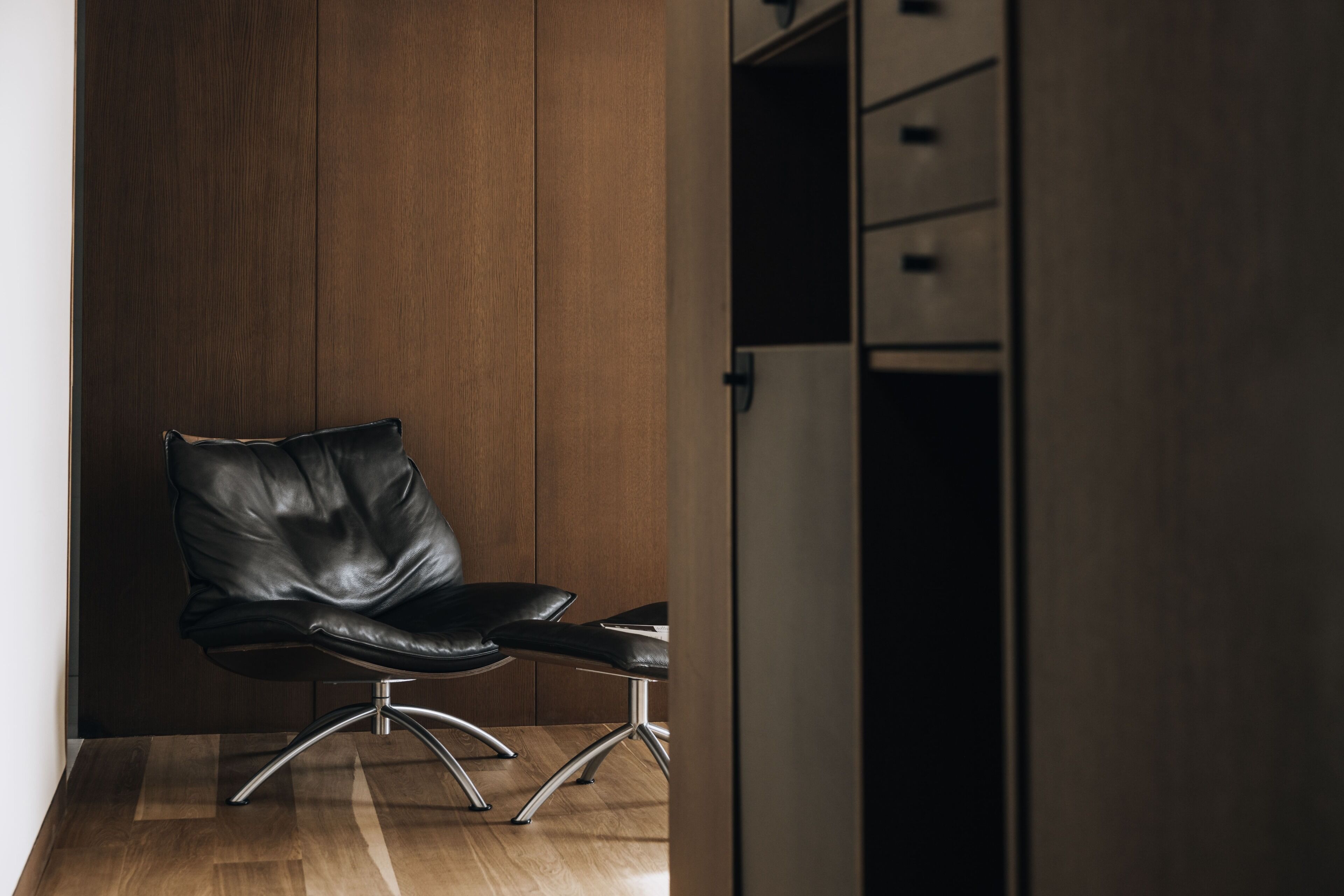 A black leather chair with a metal base, positioned in a room with wooden panel walls and a wooden floor.