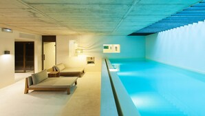 A modern indoor swimming pool with a concrete ceiling, two lounge areas with benches, and a staircase leading to a higher level. - Alma Barcelona GL (Barcelona)