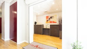 A hotel reception area with a wooden floor, a reception desk, and a modern abstract painting on the wall. - City Residence Chelles (Chelles)