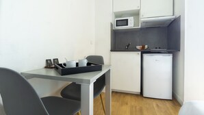 A compact kitchen with white cabinets, a microwave, and a refrigerator. There is a small dining table with chairs and a tray with cups and a spoon. - City Residence Chelles (Chelles)