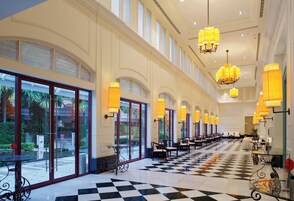 Un hall d’hôtel avec un sol à carreaux, de grandes fenêtres et de nombreux lustres.
