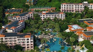 Un complejo turístico con varias edificaciones, una piscina central y exuberante vegetación circundante.