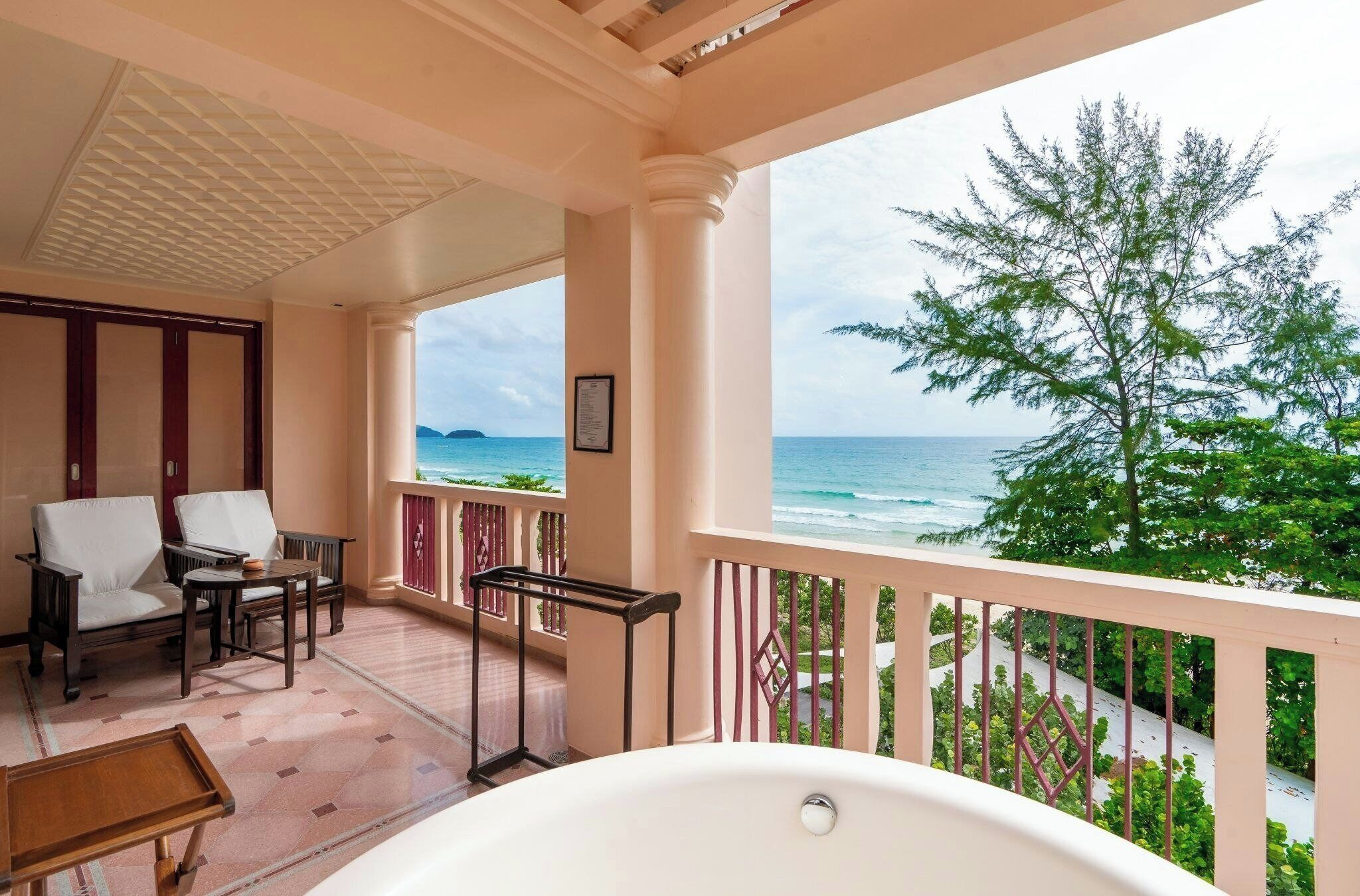 A balcony with a view of the ocean, a bathtub, and seating area with chairs and a table.