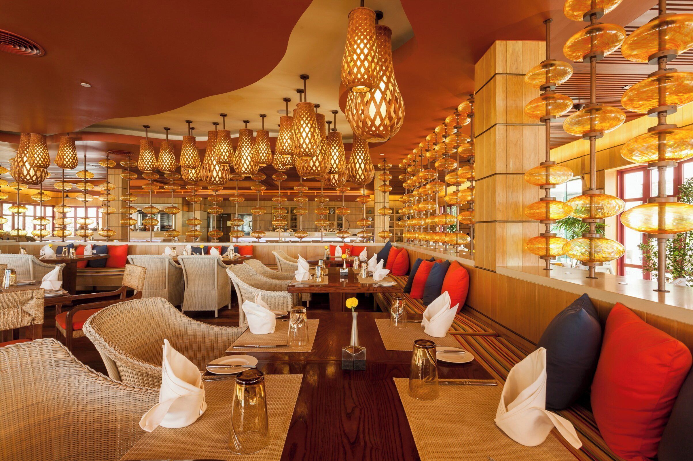 A restaurant with wicker furniture, wooden tables, and hanging lamps.