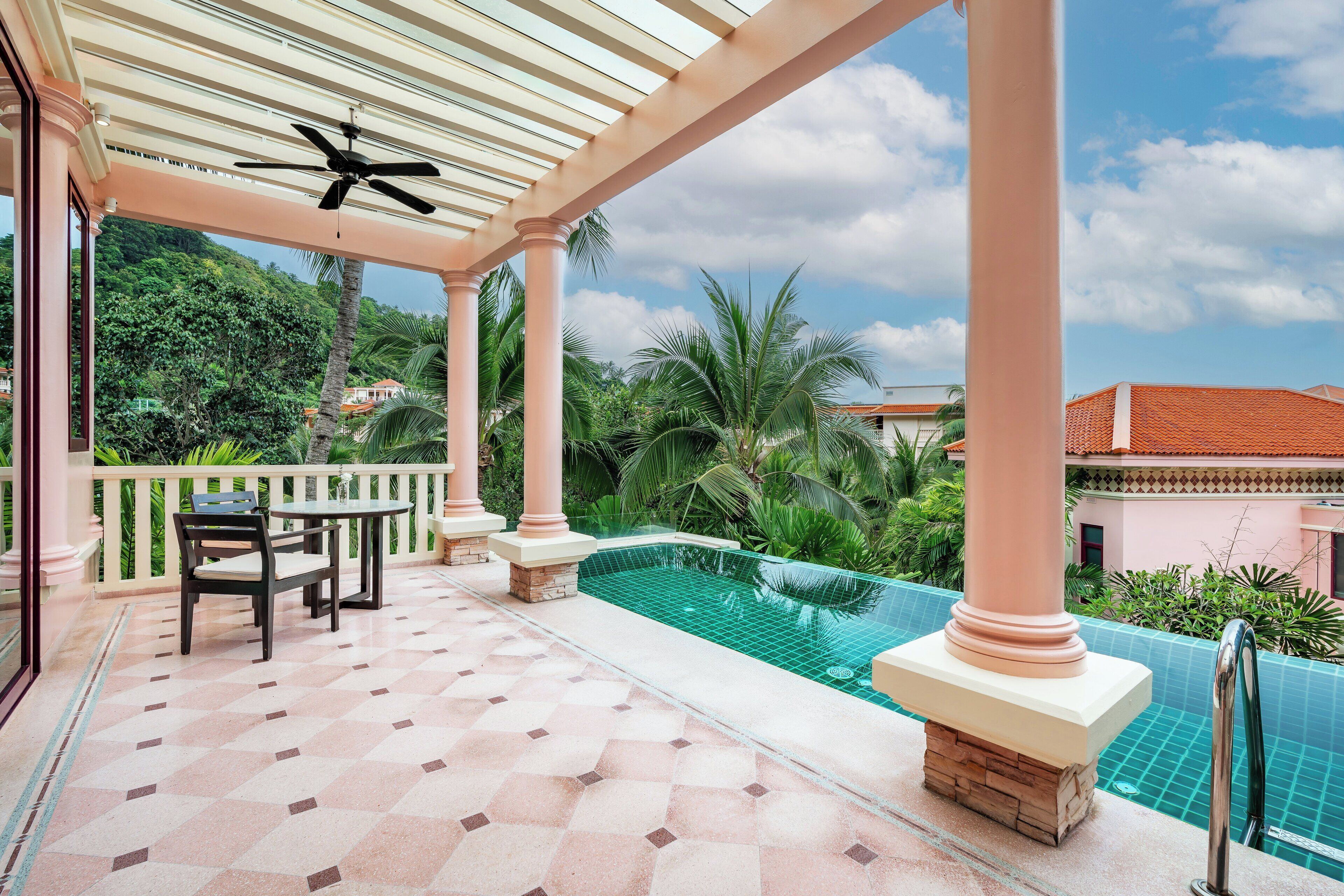 A covered outdoor area with a pool, palm trees, and a ceiling fan.
