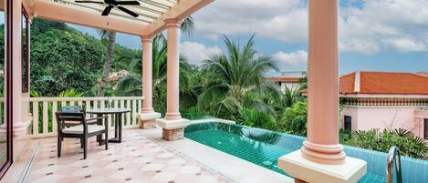 A covered outdoor area with a pool, palm trees, and a ceiling fan.