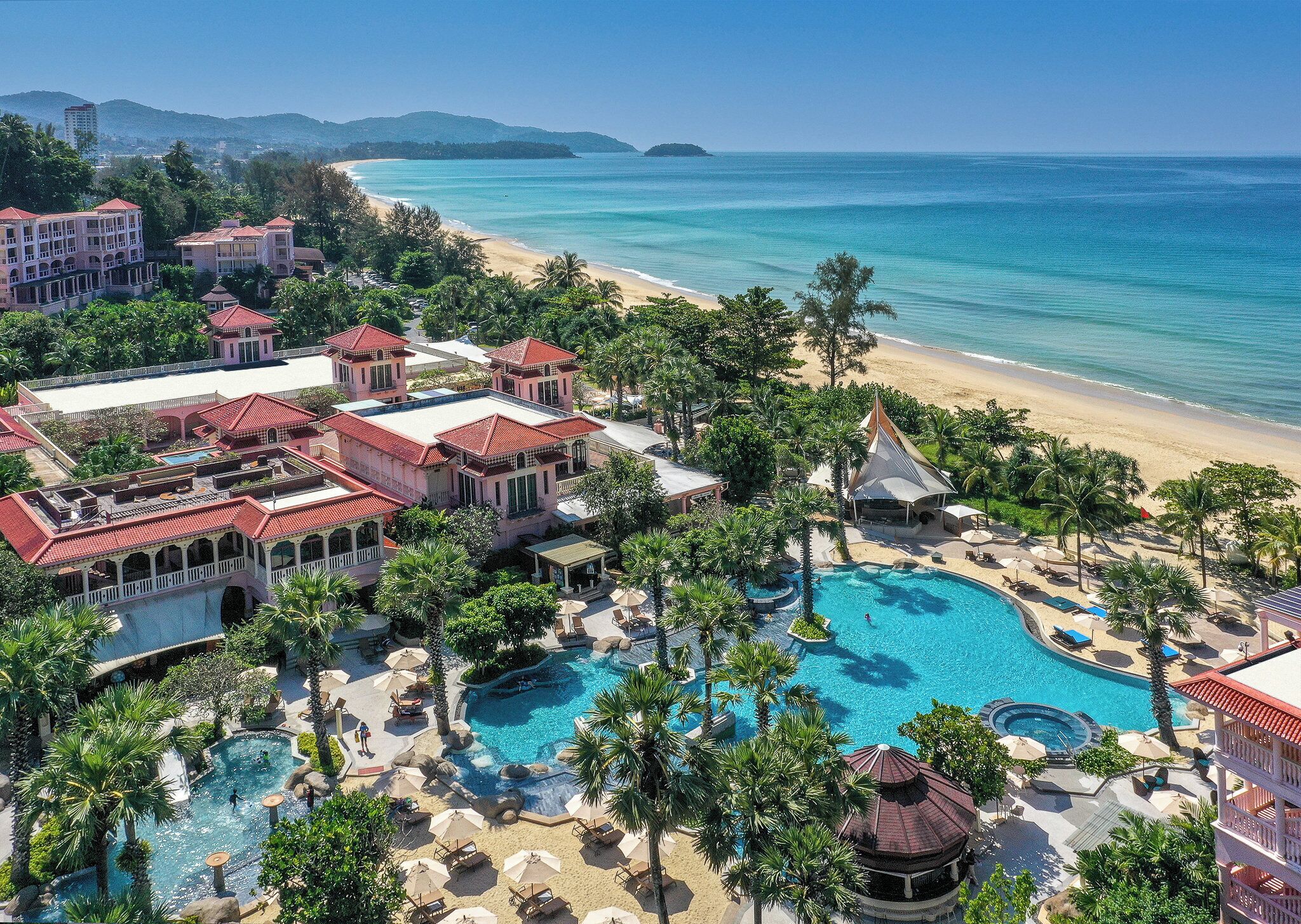 A resort with a large swimming pool, beach access, and multiple buildings with red roofs.