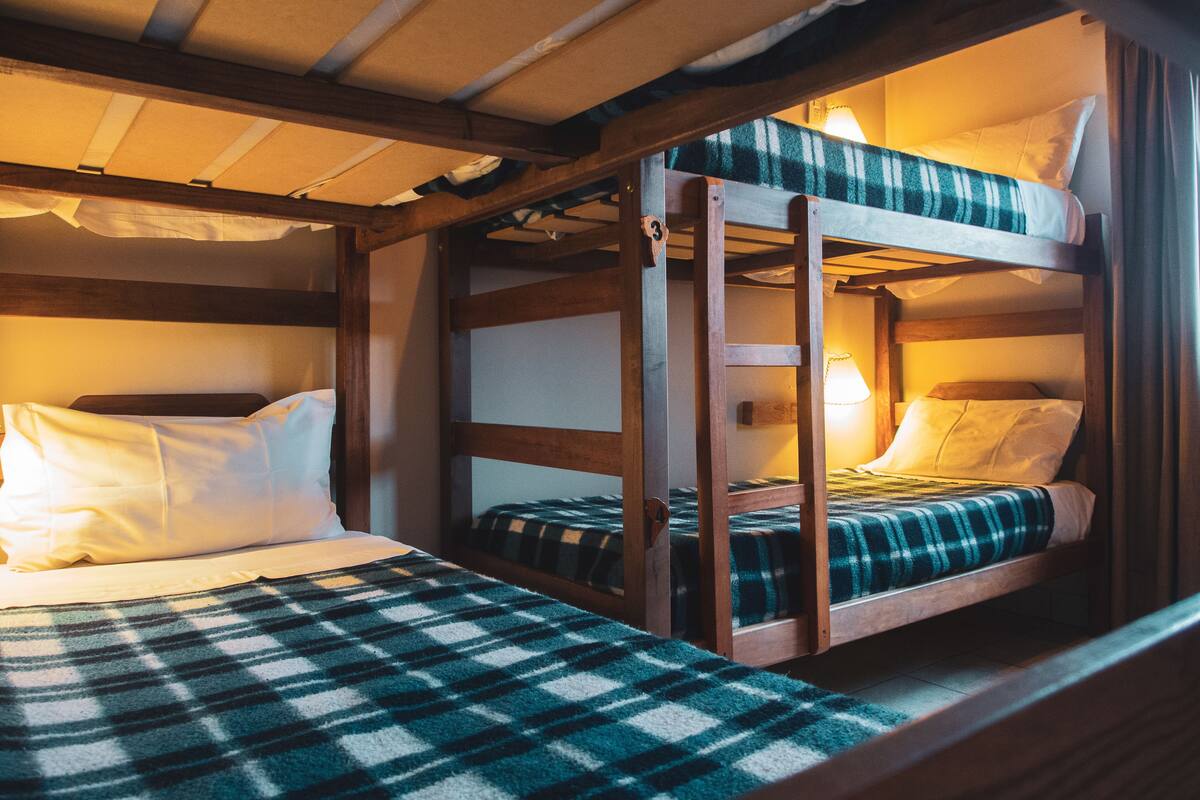 Ein Schlafzimmer mit Etagenbetten, einer karierten Decke, einem Holzkopfende und einer Nachttischlampe.
