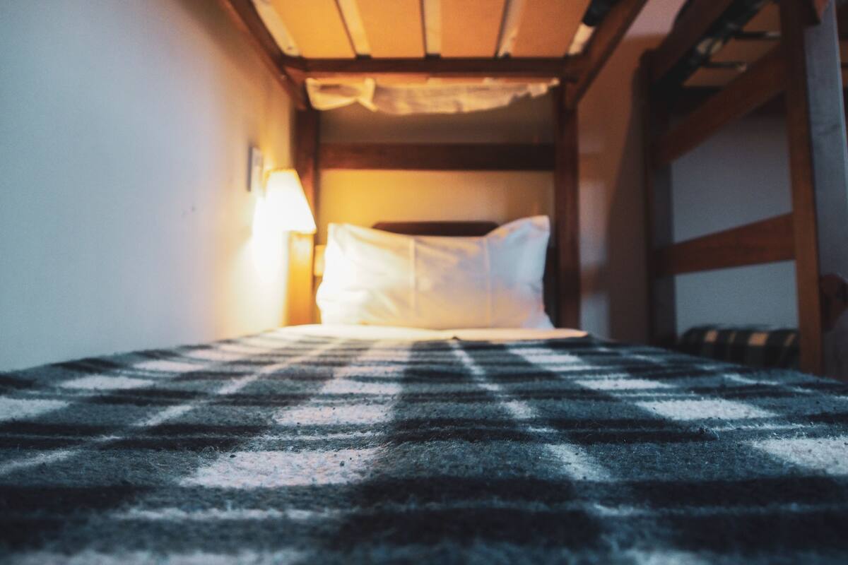 Ein Stockbett mit karierter Decke, eine Nachttischlampe und ein hölzernes Kopfstück.