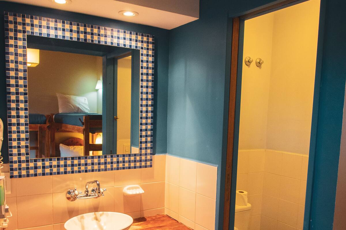 Ein Badezimmer mit einem Holzkosmetikschrank, einem weißen Waschbecken, einem Spiegel mit blau-weiß kariertem Rahmen, einer Toilette und einem Duschbereich.