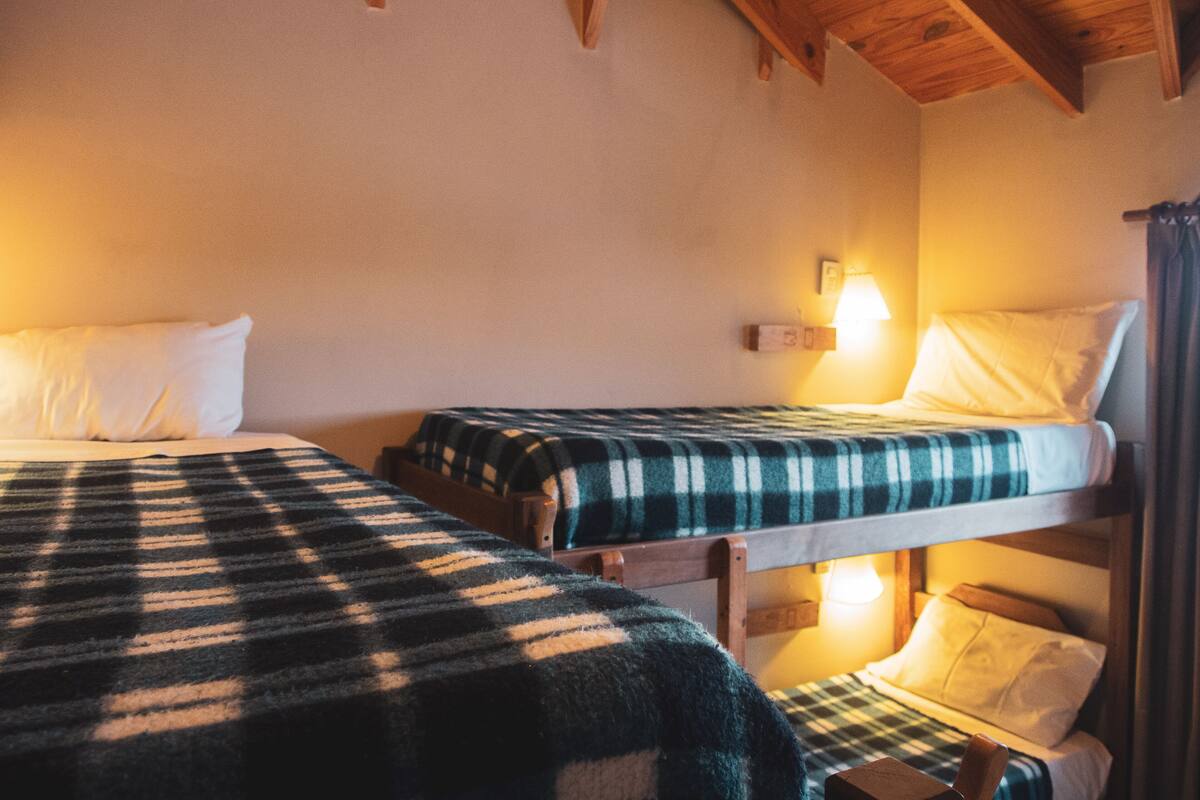Ein Zimmer mit zwei Etagenbetten, jedes mit einer Karo-Decke und weißen Kissen. Rechts an der Wand ist eine Lampe befestigt.