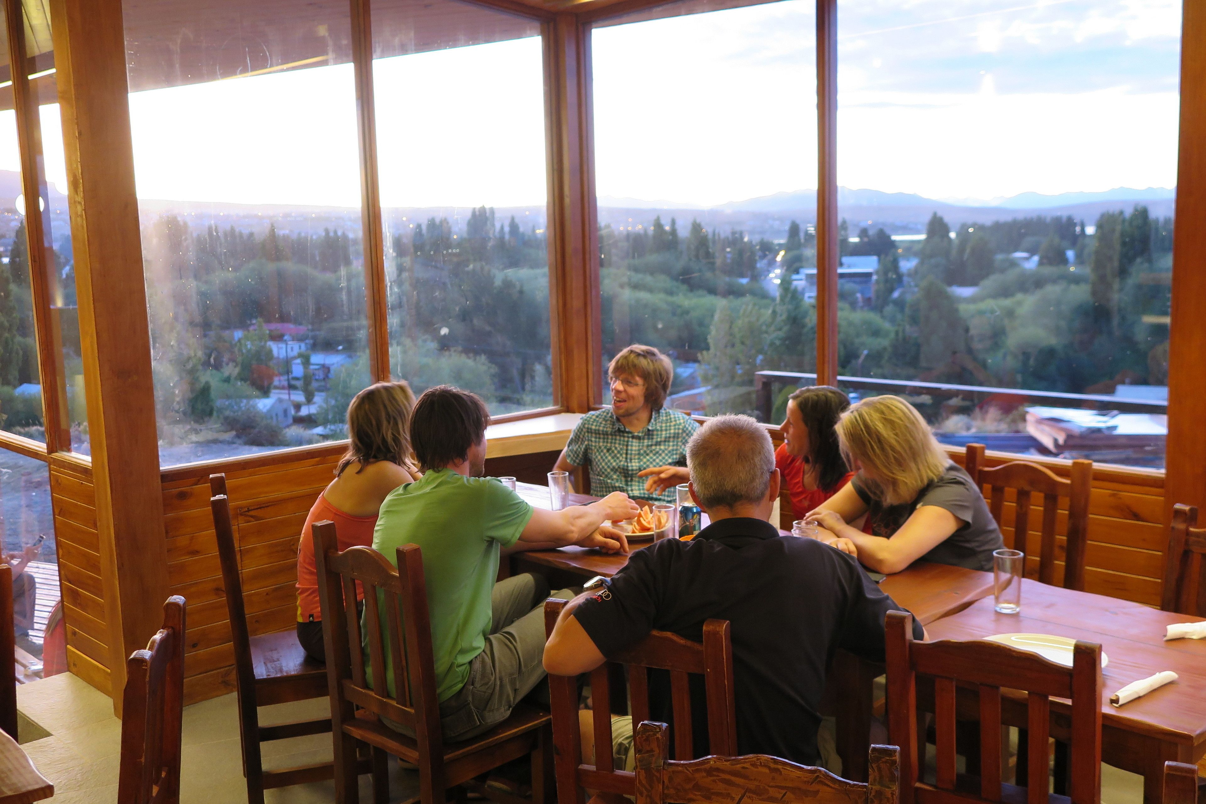A group of people dining at a wooden table with a view of a forested landscape through large windows.