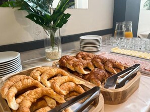 A breakfast buffet with croissants, cheese, and juice. - Hotel Alpino (Buenos Aires)
