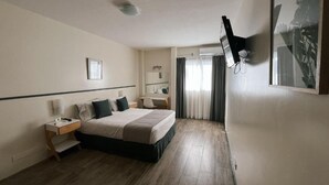 A hotel room with a bed, bedside table, lamp, and a wall-mounted TV. - Hotel Alpino (Buenos Aires)