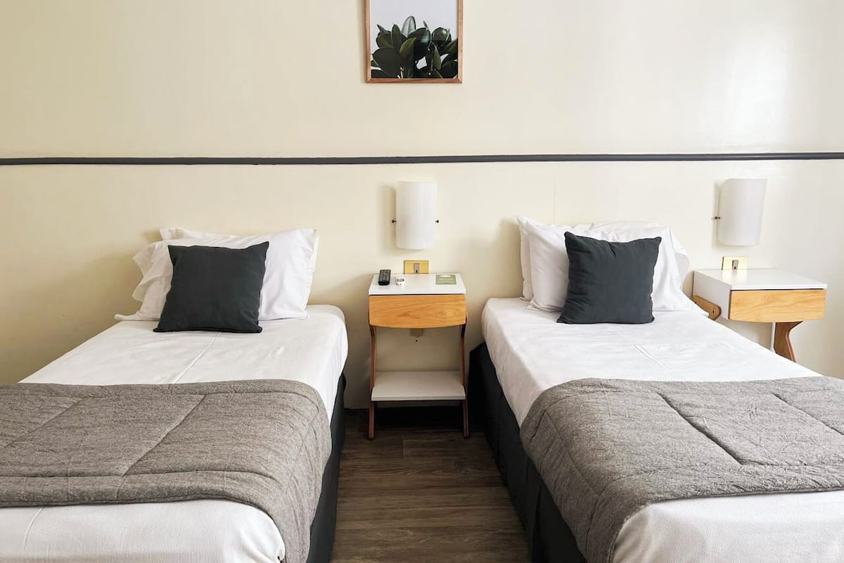 A hotel room with two single beds, each with a pillow, bedside tables, and lamps.