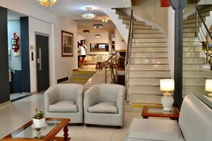 A hotel lobby with a staircase, two armchairs, a coffee table, and a television in the background. - Hotel Alpino (Buenos Aires)