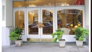A hotel entrance with a glass door, potted plants, and a reflection of a car and street in the window. - Hotel Alpino (Buenos Aires)