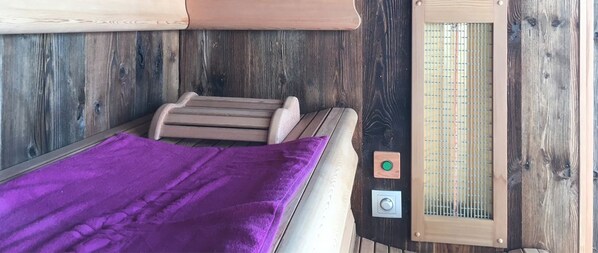 A small, cozy room with a wooden wall, a bench, a purple blanket, and a window with a grid pattern.