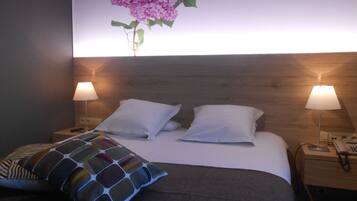 A hotel room with a wooden headboard, two white pillows, a colorful throw pillow, a bedside lamp, and a phone on the nightstand.