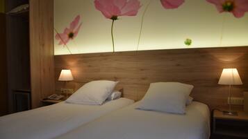 A hotel room with two beds, wooden headboard, white bedding, and a wall with pink flowers.