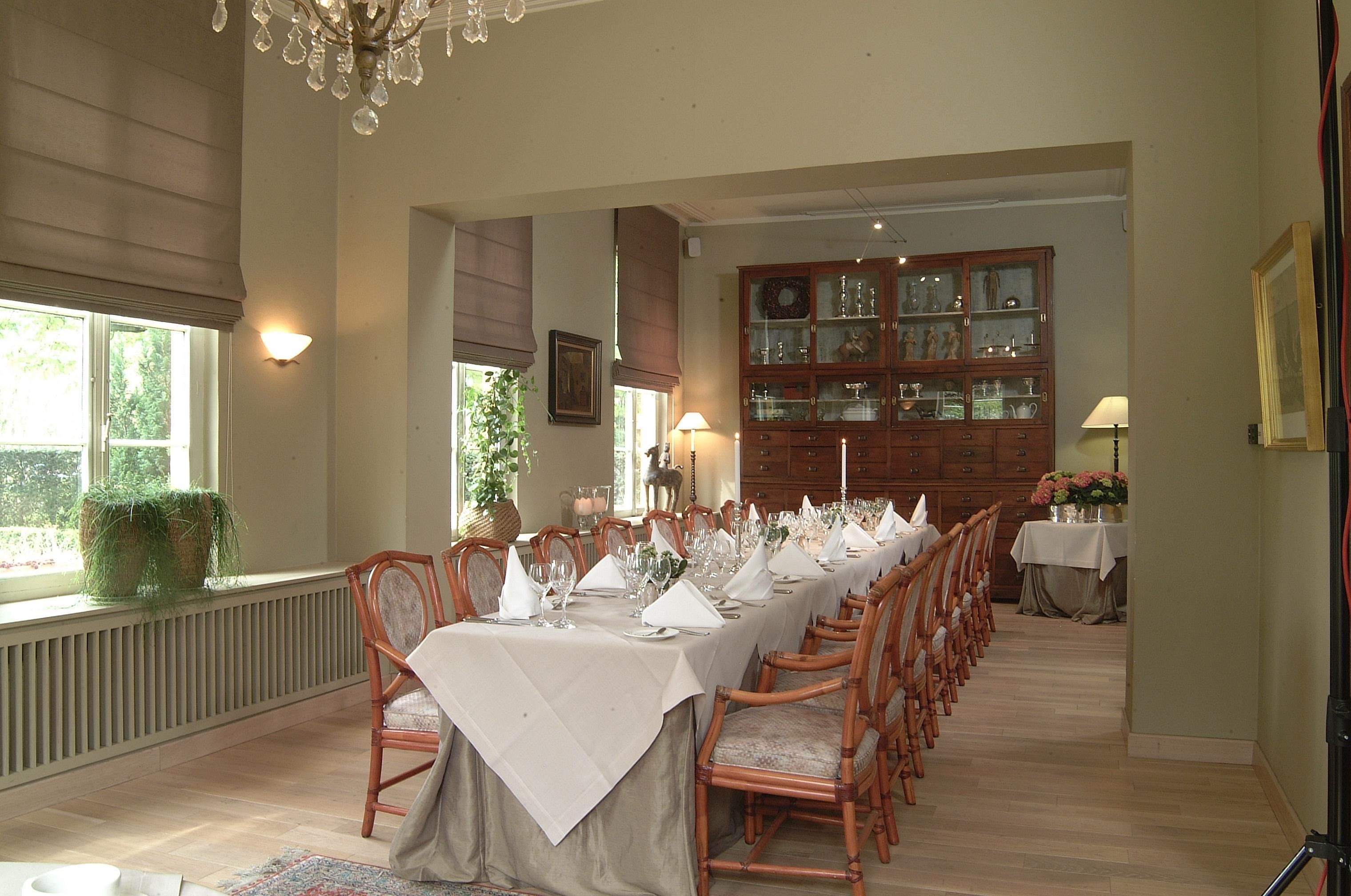 A dining room with a long table set for a meal, wooden chairs, a chandelier, and a cabinet with glass doors.