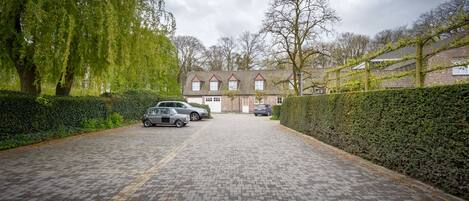 A paved driveway leading to a house with a brick facade and a tiled roof.