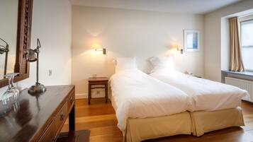 A hotel room with two beds, a wooden dresser, a mirror, and a nightstand with a lamp.