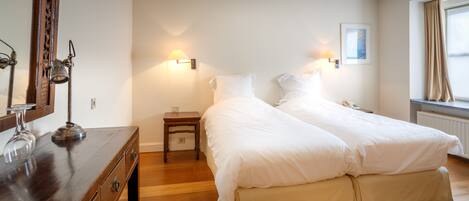 A hotel room with two beds, a wooden dresser, a mirror, and a nightstand with a lamp.